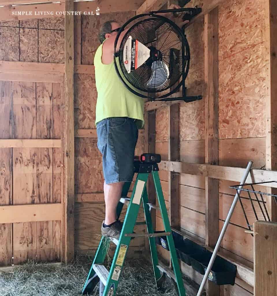 a man putting up a fan in a barn 
