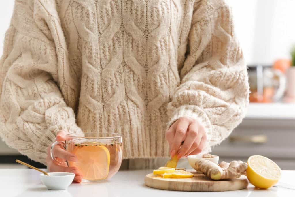 A woman in a cream sweater with a cup of tea in her hand and a lemon slice in the other