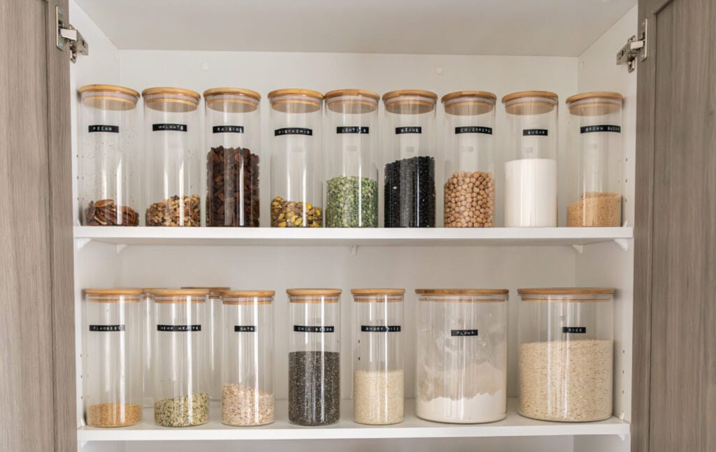 Pantry shelves with labeled glass jars filled with various nuts, grains, and pantry staples
