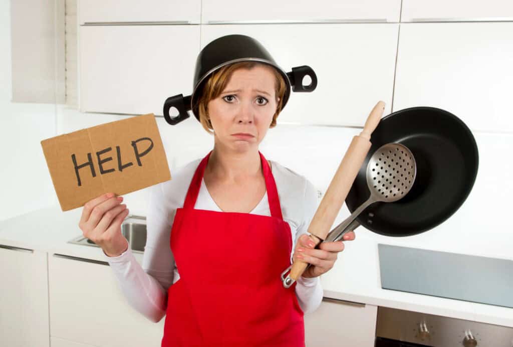 a woman in a red apron holding a sign that says help with a pot on her head in a kitchen 