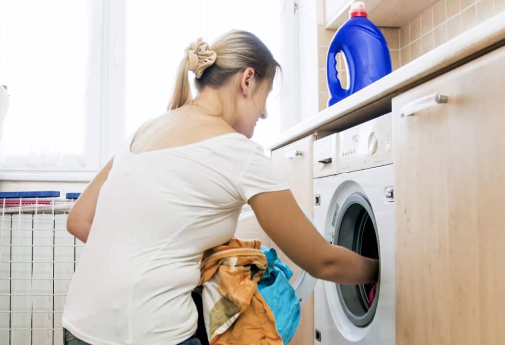 a woman putting clothes into a washing machine 