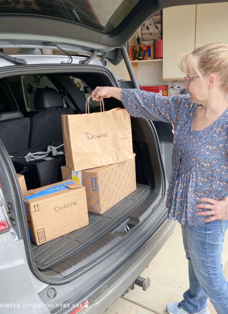 A midlife woman putting a donation bag into a the trunk of her car