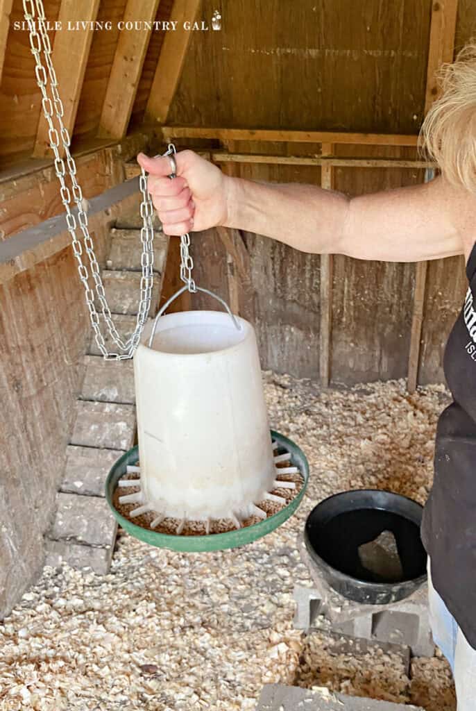 a woman holding a feeder in a chicken coop