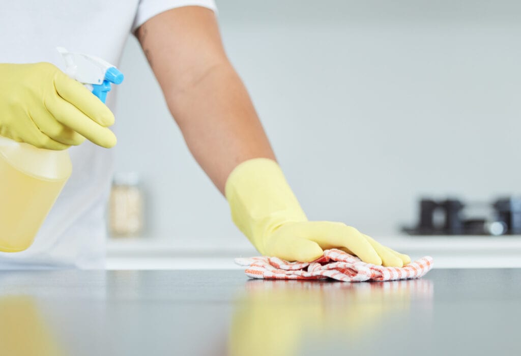 hands spraying lemon water onto a kitchen counter to prevent fruit flies