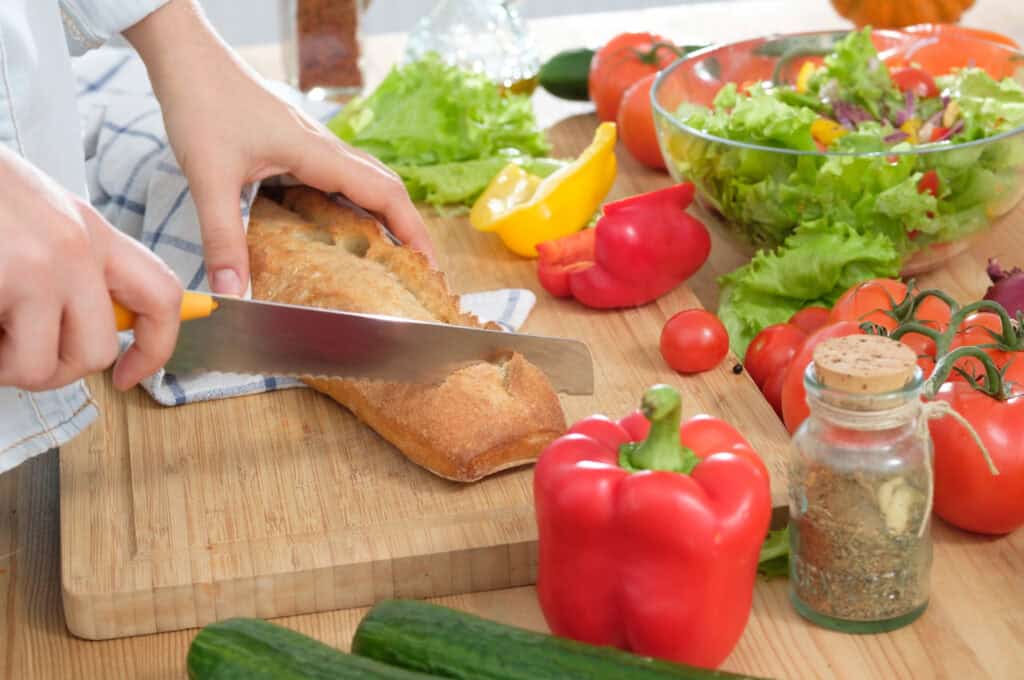 hands using a knife to cut a loaf of fresh bread 