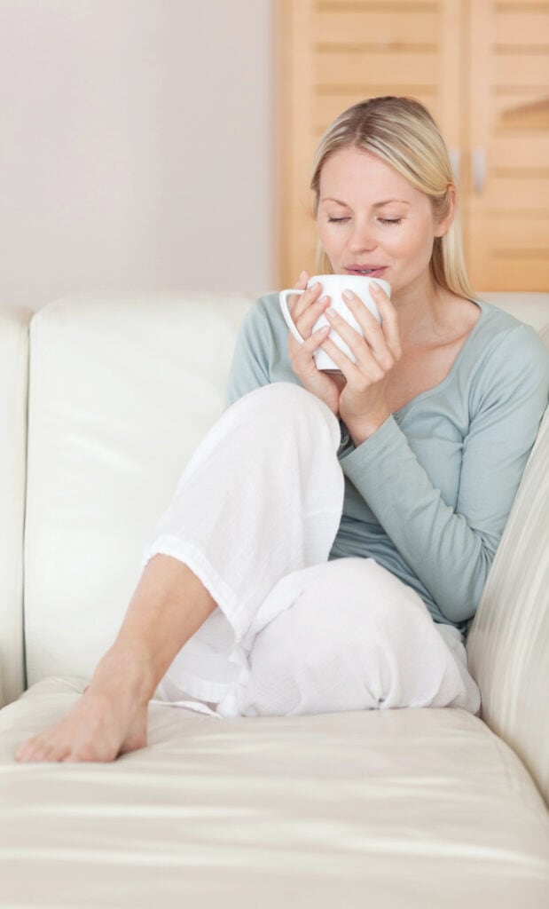 a midlife woman relaxing on a couch with a cup of coffee
