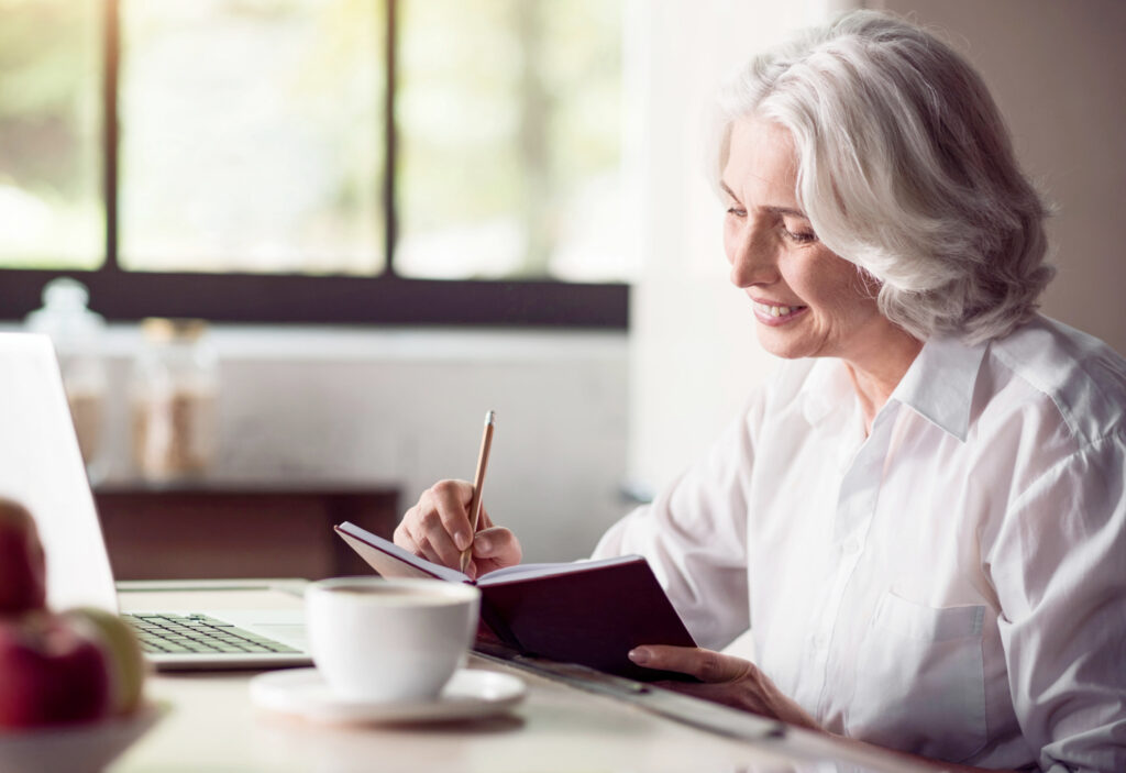 a woman writing a to do list in a book near to a computer (1)