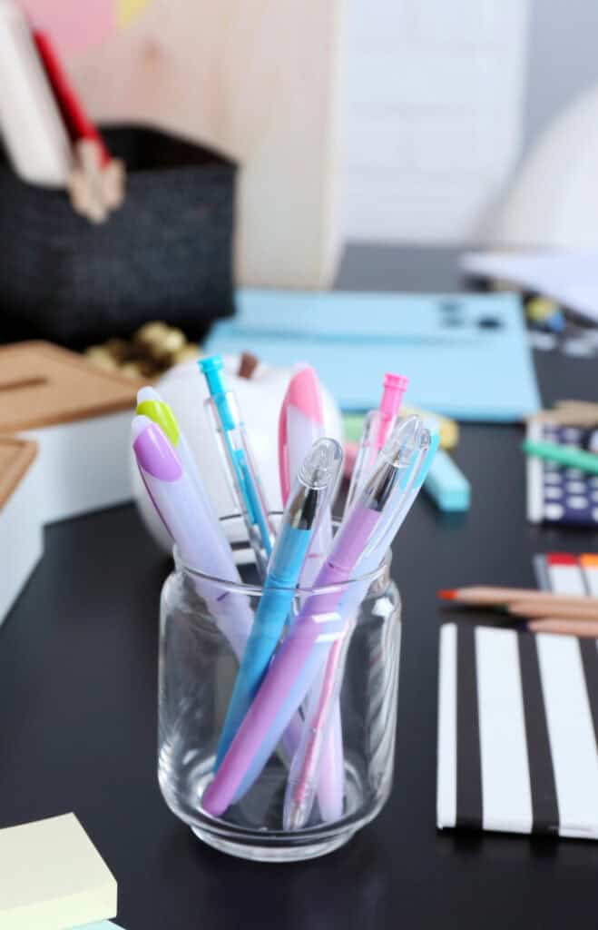 a glass jar on a desk with pens inside